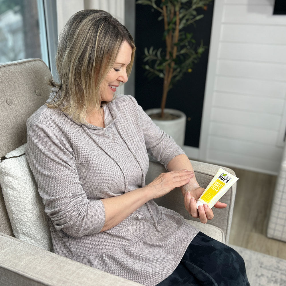 Woman sitting in chair applying Doctor Hoy's Arnica Boost Recovery Cream to aching wrist