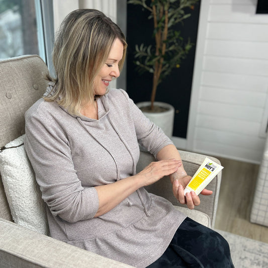 Woman sitting in chair applying Doctor Hoy's Arnica Boost Recovery Cream to aching wrist