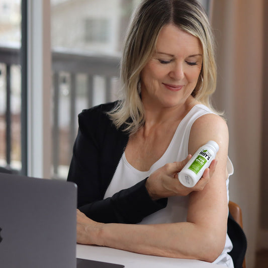 Woman working at desk with computer, applying Doctor Hoy's Natural Pain Relief Gel to aching shoulder